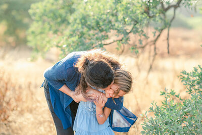 Mom hugging her young daughter in a field in San Diego
