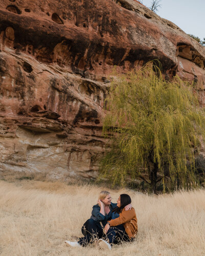 LGBTQ+ couple smiles together at their red rocks engagement session