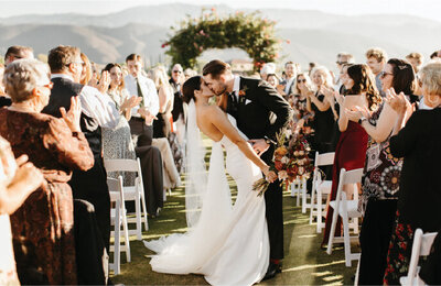 groom and bride kissing while wedding party cheers