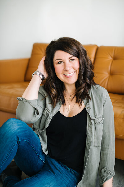 A smiling woman sitting on the floor in front of a modern couch