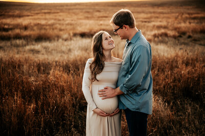 Man holds woman's pregnant belly in long flowy dress in field