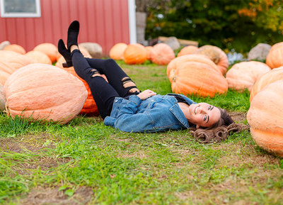 high school senior girl laying on ground in pumpkin patch with legs propped up on pumpkin