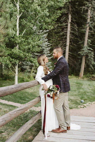 Bride and groom stand with foreheads together in front of a lake