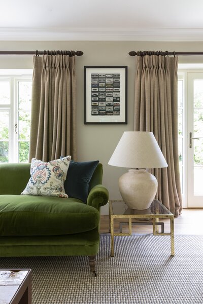 Green sofa in living room with beige curtains and lamp on table