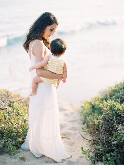 A mom holds her baby and looks out at the ocean in Malibu
