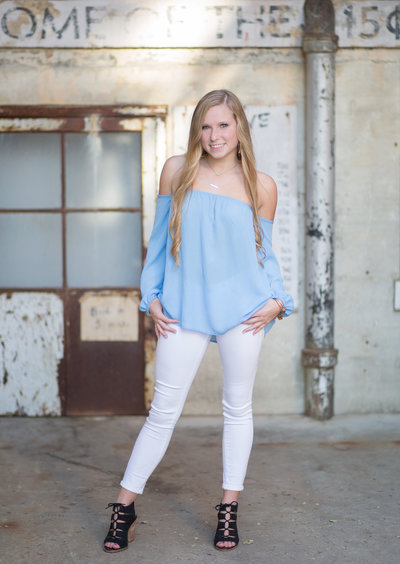 High school senior girl poses for photo in blue shirt and white jeans