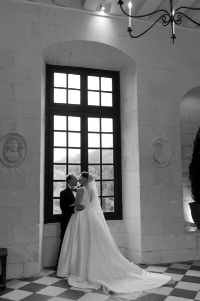 photo of man and woman embracing in front of a large window at a castle in france