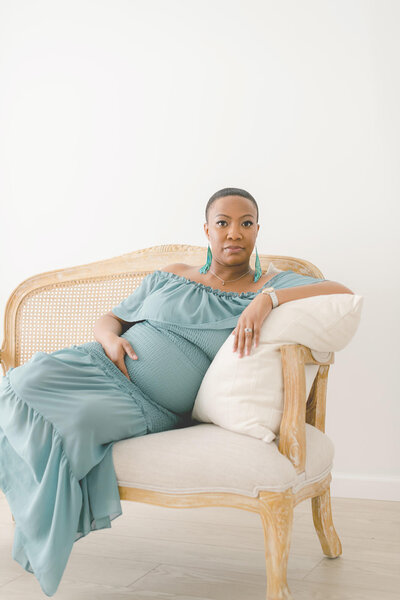 Pregnant woman sitting on a settee wearing an aquamarine fitted dress and long dangle aquamarine earrings