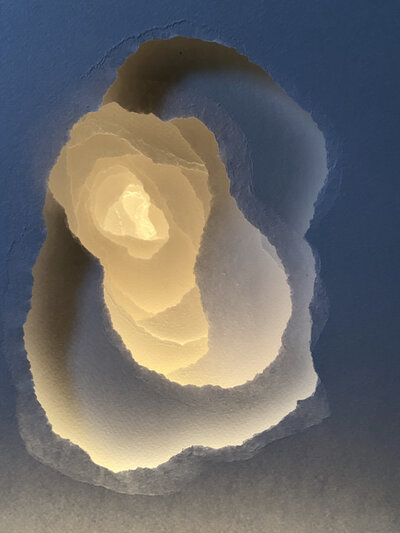 Layers of white paper illuminated from inside torn holes. Art by Angela Glajcar.