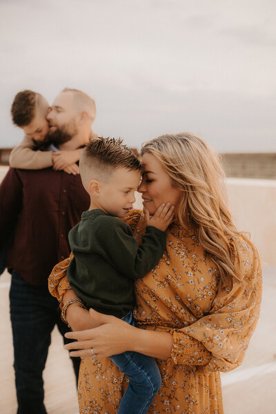Mom holding her son while he holds her face and his father holds his brother in the background.