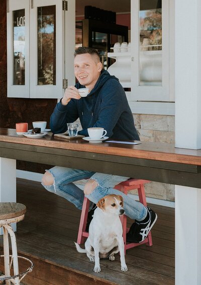 About Photo of Chris Perkins, underatreehouse Photographer drinking coffe at Lords of Pour, Ettalong, Central Coast NSW with his dog. Smiling and happy.