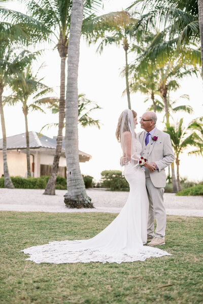 bride and groom standing facing each other and holding hands with palm trees in the background