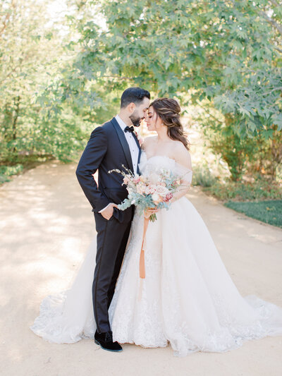 bride and groom with heads together on a path under trees