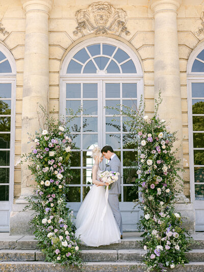 Bride and groom at beautiful outdoor chateau French destination wedding under floral arch