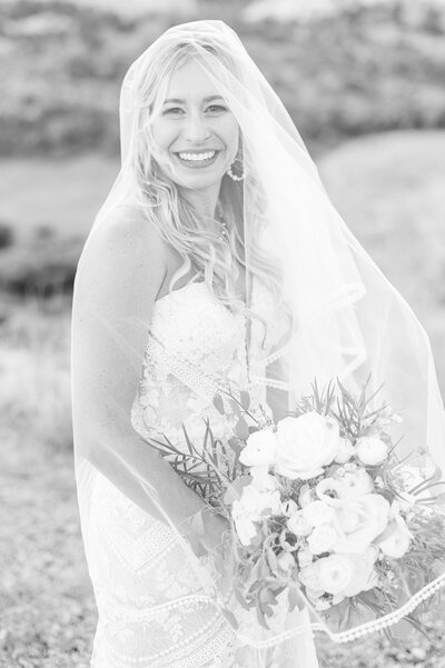Smiling bride holding her bouquet under her veil on Mesa Overlook.