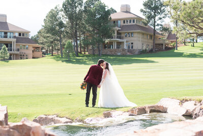 Denver wedding photographer captures bride and groom on a golf course in Denver holding ahnds and kissing ona field for their summer wedding