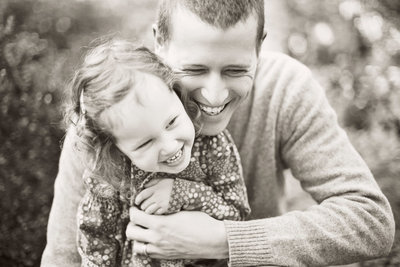 father hugging young daughter from behind while they laugh