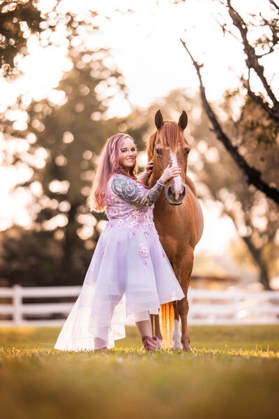 photo of katy of katy in design in a purple dress smiling at the camera next to her chestnut horse with her hand on the horse's nose
