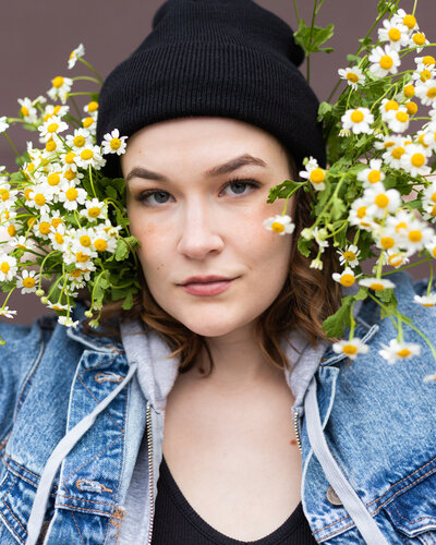 person in a black beanie with two sets of flowers on either side of their face