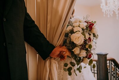 A large bouquet of bridal flowers and a man and women holding hands separated by a curtain on their wedding day.