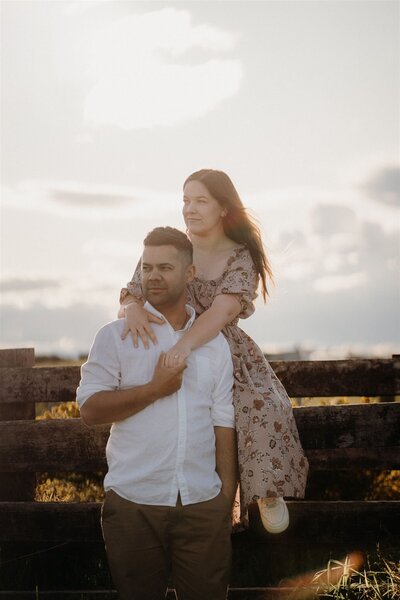 A couple sitting on a fence at sunset during their engagement photoshoot with photographer Tashina Narelle