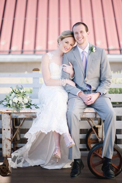 Bride and groom sit atop a rustic table next to their bouquet