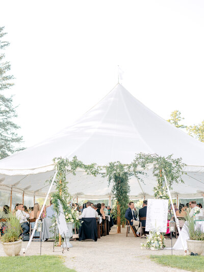 White reception tent draped with greenery with guests sitting at tables underneath
