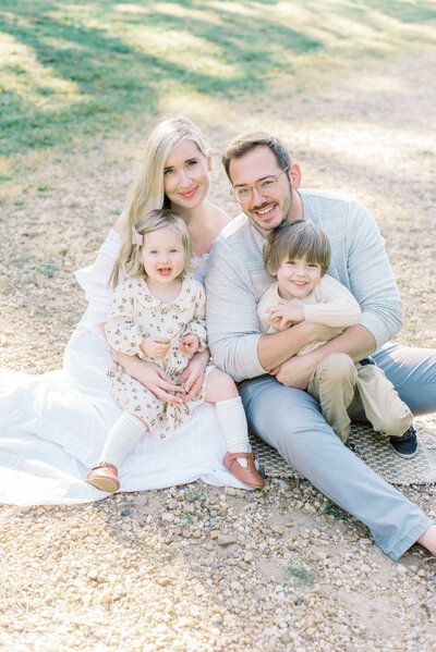Fine Art Photographer Marie Elizabeth Photography sitting on a gravel pathway with her husband and her two young children on her lap