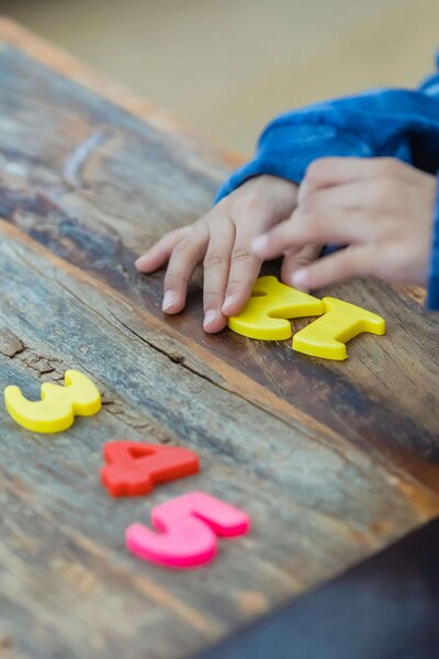 A child is playing with colorful plastic numbers on a wooden surface, arranging them in order while focusing on a yellow number "4."