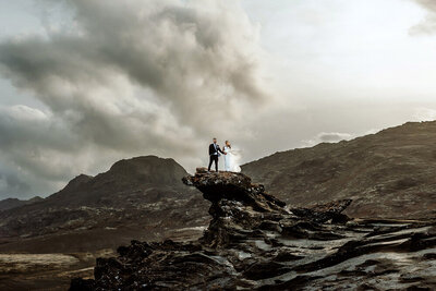 Couple is standing on the top of a cliff in Iceland surrounded by mountains
