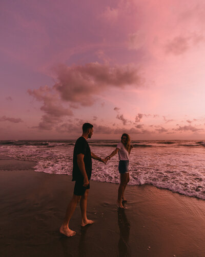 man and woman walking on sand next to ocean