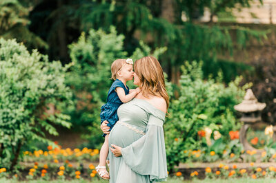 An expecting mama getting her nose kissed by her toddler at the Alberta Legislature gardens