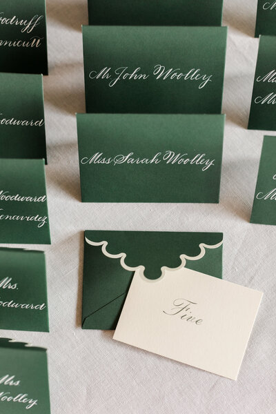 Green wedding escort card display with white handwritten calligraphy script