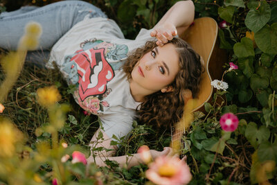 girl laying in field with guitar in rolling stones tshirt