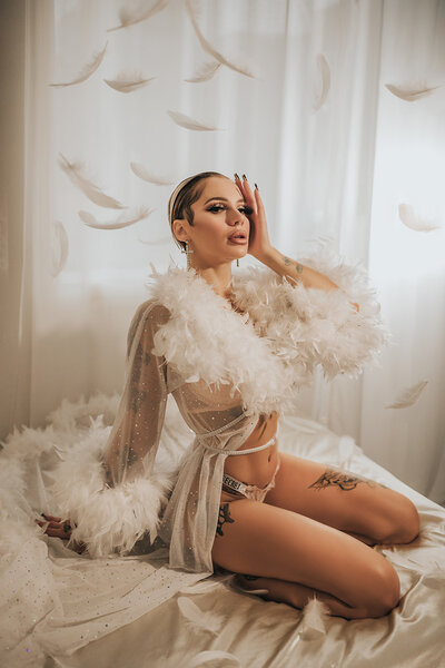professional dancer Demi Reign kneeling on a bed surrounded by feathers at her boudoir photoshoot