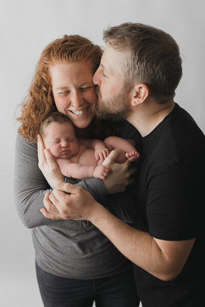 newborn baby girl with parents holding her and kissing and laughing