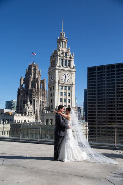 Bride and groom photo on a rooftop in downtown Chicago that show The Wrigley Building  tower in the background.