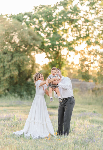 A maternity photography session taken by Bay area photographer shows an expecting mother caressing her baby bump in a field of almond blossoms with her partner.