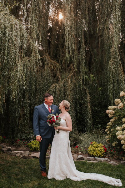 Bride and groom standing under willow tree