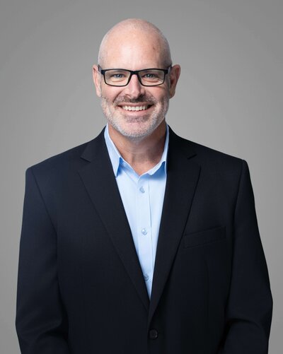 Modern professional headshot of Jon against a neutral gray background, showcasing clean lighting and confident expression captured by Liza Hondros Photography.