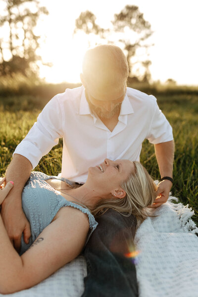 Engagement photos in a field laying down with sun peaking behind them