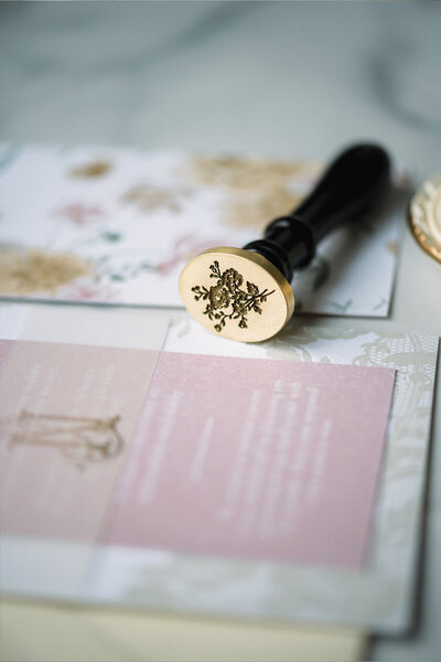 Intricate view of a floral oval wax seal with deep engraving, elegantly placed on top of a pink and yellow letterpress baby shower invitation.