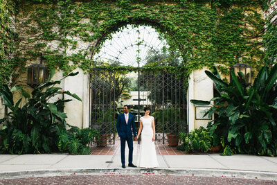 Stylish bride and groom pose in front of ivy covered gate on their wedding day