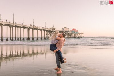 Engaged couple cozy up on the beach next to the Huntington Beach Pier
