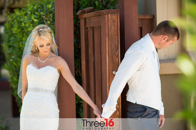 Bride and Groom hold hands as they are separated by a door so they don't see each other before the ceremony as they pray together