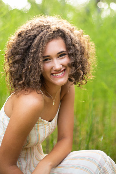 Teen girl smiles for the camera outdoors during senior portraits