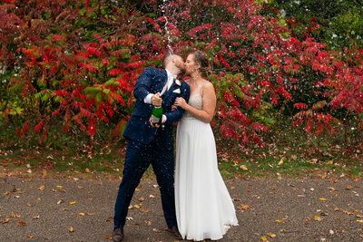 Bride and groom spray champagne in front of flowers on wedding day.