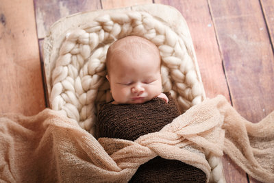 Beautiful Mississippi Newborn Photography: sleeping newborn boy  wrapped in brown in a wooden dough bowl
