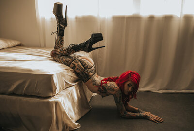 tattooed boudoir photography client posing in red light with a crop whip