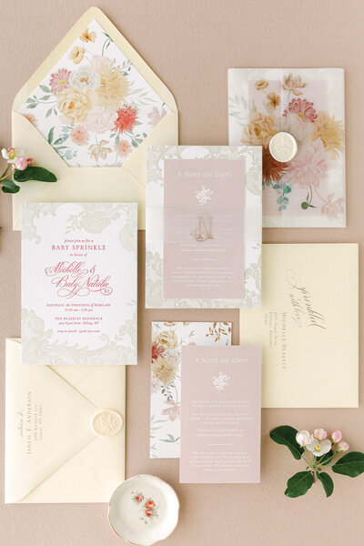 Elegant pink and yellow baby shower invitation suite featuring two-color letterpress with lace detailing border, floral envelope liner, monogram vellum belly band, and wax seals.